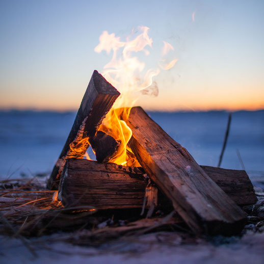 Ein Haufen mit brennendem Holz am Strand und Meer im Hintergrund.
