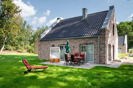 Rotes Backstein-Ferienhaus mit einer gepflasterten Terrasse, auf der Gartenstühle und ein klassischer Strandkorb zum Entspannen einladen.