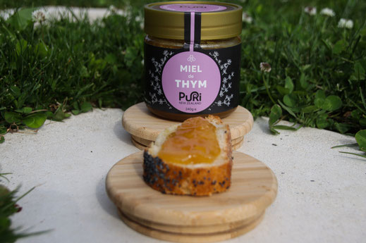 Miel de thym nouvelle-zélande 240g Puri New Zealand sur un bouchon en bois dans un jardin avec une tartine de pain grillé avec Miel de thym dessus
