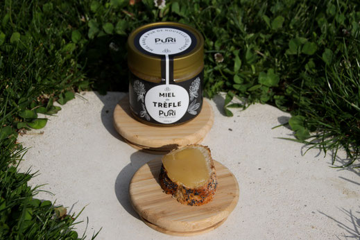 Miel de trèfle nouvelle-zélande 240g Puri New Zealand sur un bouchon en bois dans un jardin avec une tartine de pain grillé avec Miel de trèfle dessus