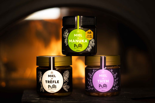 Photo de trois Miels de Nouvelle-Zélande en pot de 240g de Miel de Manuka, Thym et Trèfle Blanc de Puri New Zealand hiver avec les flammes d'une cheminée en arrière plan