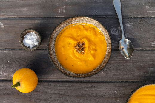 A handmade ceramic bowl filled with winter pumpkin soup served on a wooden table
