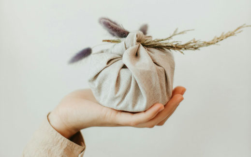 Een hand die een pakket vasthoudt, ingepakt in een doek en versierd met een droogbloem en takje