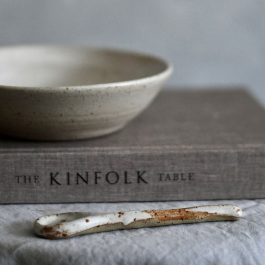 Handmade ceramic bowl on top of a Kinfolk book, on a tablecloth with a ceramic teaspoon in front of the book