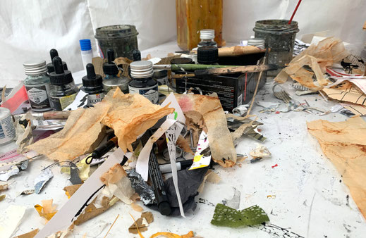 Authentischer Blick auf den Arbeitstisch im Dortmunder Atelier von Claudia König. Zu sehen ist der kreative Prozess mit Tuschegläsern und Schichten aus gefundenen Papieren und Fragmenten für die Collage-Arbeiten.
