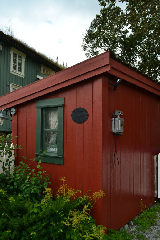 De oude telefoon op een rood gebouwtje aan het water. 