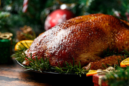 krosse, rot-braun gebratene saftig glänzende Gans auf schwarzem Teller mit Weihnachtsdekoration wie Tannenzweigen sowie Orangenscheiben