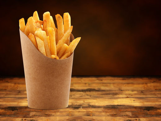 Eine klassische Portion goldgelber Pommes in der Papiertüte auf einem Tisch