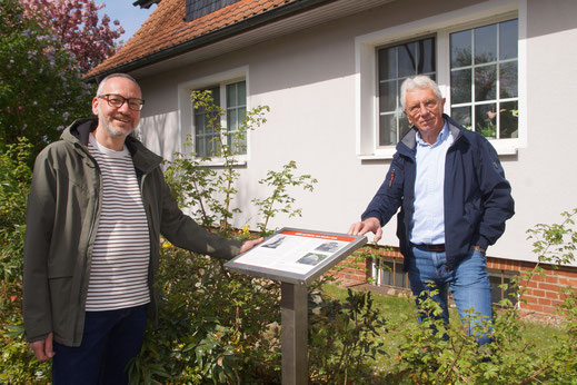2 Männer stehen bei einer Gedenktafel vor einem Haus