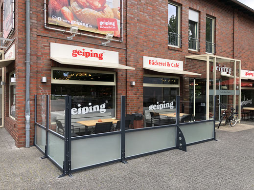 Bäckerei-Terrasse mit rotem Großschirm, transparenten Glas-Windschutz-Elementen und Außenbestuhlung