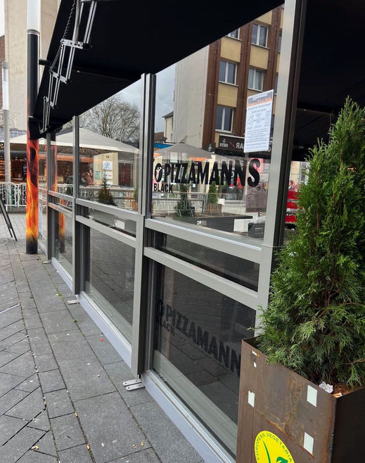 Höhenverstellbare Windschutzwand in klarem Glas unter einer Scherenarm-Markise