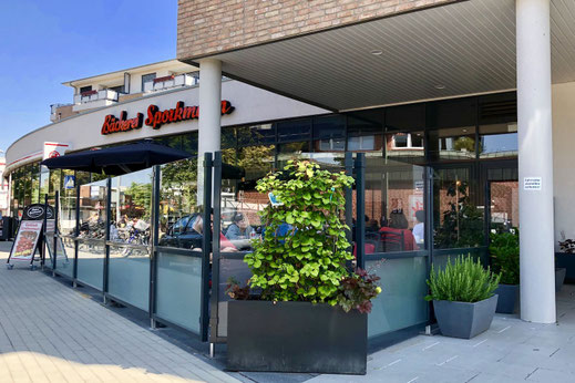 Glas-Windschutz mit dunklem Rahmen an der Außenterrasse einer Bäckerei