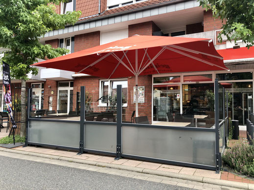 Bäckerei-Terrasse mit rotem Großschirm, transparenten Glas-Windschutz-Elementen und Außenbestuhlung