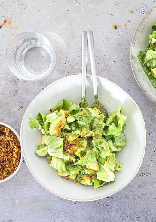 Knusprige Reis-Bowl mit Endiviensalat, Avocado und Gurke, serviert mit cremigem Dressing auf einem hellen Teller