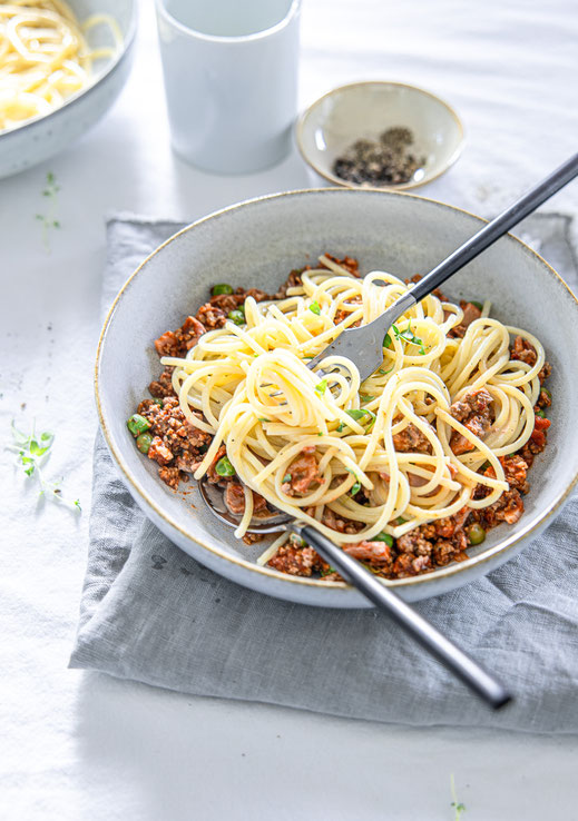 Mediterrane Hackfleisch-Spaghetti mit frischen Kräutern, Erbsen und cremiger Sahnesauce auf einem weißen Teller serviert