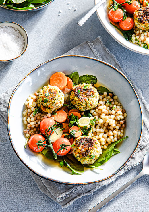 Klare Gemüsesuppe mit knusprigen Gemüsebällchen, Fregola und Babyspinat in einem Suppenteller