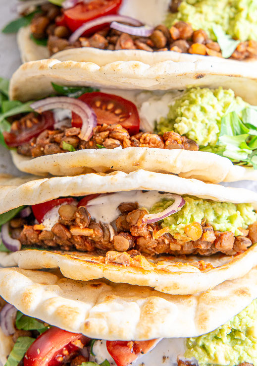 Gefüllte Tacos mit Tellerlinsen, Avocadopüree, Kirschtomaten, roten Zwiebelringen und Joghurt