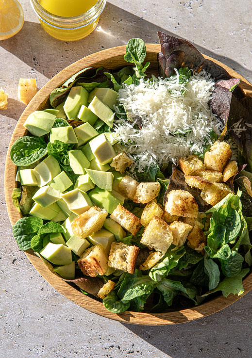Knackiger Blattsalat mit gerösteten Ciabatta-Würfeln, Avocado und frisch geriebenem Parmesan, serviert in einer Holzschale.