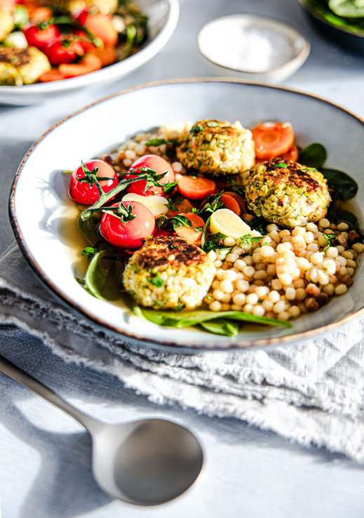 Klare Gemüsesuppe mit knusprigen Gemüsebällchen, Fregola und Babyspinat in einem Suppenteller