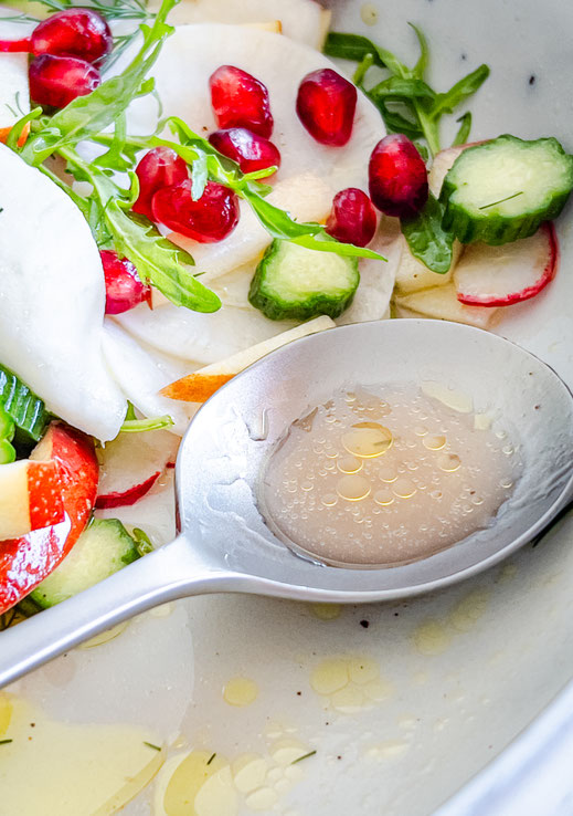 Rettichsalat mit Radieschen, Minigurke und Granatapfelkernen in einer weißen Schüssel angerichtet - mit Dill-Vinaigrette angemacht und frischem Dill als Topping
