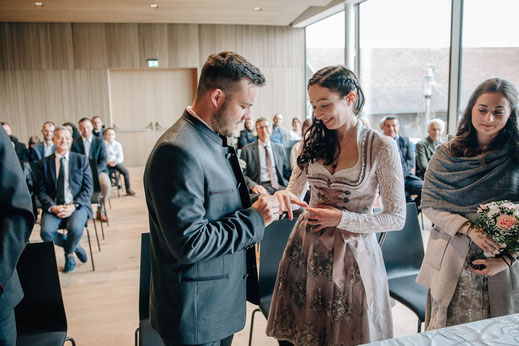 Hochzeit Sistrans Standesamt Trauung Bräutigam steckt Braut den Ring an den Finger Gäste im Hintergrund