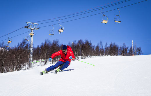 Man in front of ski lift in red jacket sking fast