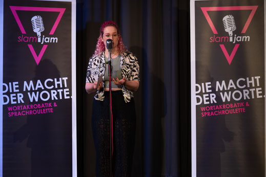 Poetry Slam Künstlerin Katharina Marosz am Mikrofon auf einer Bühne.
