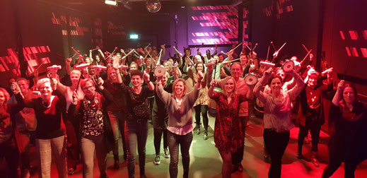 Deelnemers bespelen trommels en tijdens een actieve percussie workshop