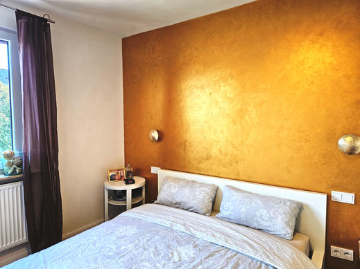 Eine einzelne Wand ist mit einem goldfarbenen Material verputzt. Die anderen Wände sind weiß verputzt - mit Lehm