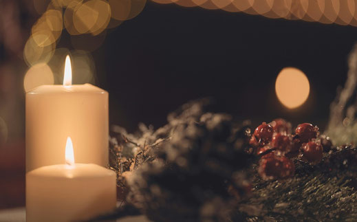 Auf dem Bild ist eine Kerze neben einem Tannenzweig zu sehen.