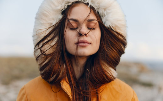 Das Bild zeigt eine Frau, die am Strand steht. Sie atmet bewusst ein und entspannt.