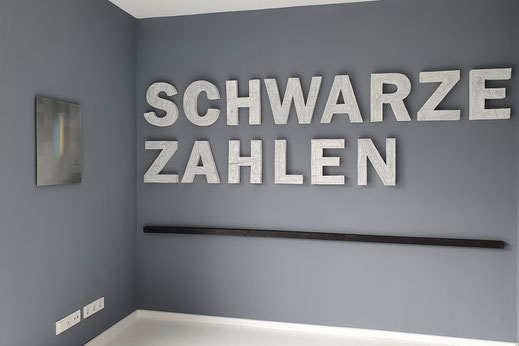 SCHWARZE ZAHLEN, Bilanz der Wahrheit ist eine Arbeit von Oliver Braig. Ein schwarzer Strich aus Holz, deutet eine Abrechnung an. Was ist unterm Strich, was kommt dabei heraus? Wer bezahlt hier wen für was? Wer bezahlt was und warum? Schwarz und weiß kann 