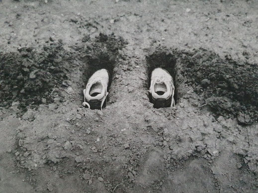 Auf der dritten Photographie sind Braig's Turnschuhe zu sehen, die im Feld in der Erde so eingegraben sind, dass sie mit der Erdoberfläche fast bündig sind. Links und rechts der Schuhe, liegt der Aushub. Der Künstler Oliver Braig nutzt die Perspektive um 