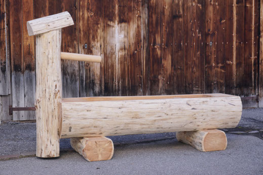 Brunnentrog aus Lärchen-Rundholz mit Brunnenstock vor einer alten Holzscheune.