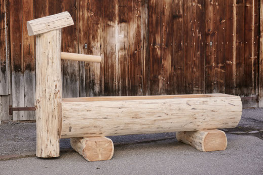 Brunnentrog aus Lärchen-Rundholz mit Brunnenstock vor einer alten Holzscheune.