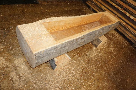 Brunnentrog aus Lärchen-Rundholz während der Herstellung mit sichtbarer Holzstruktur und Hobelspänen.