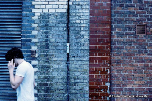 Verschiedene Materialien an der Wand, Junger Mann telefoniert im Vorbeilaufen