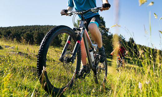 Teil eines Fahrradfahrers aus Froschperspektive, dahinter noch ein Radfahrer, auf einer Wiese