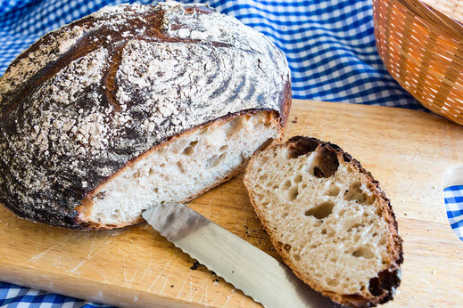 Weizensauerteigbrot rund angeschnitten auf Holzbrett und blau weiss karierter Decke