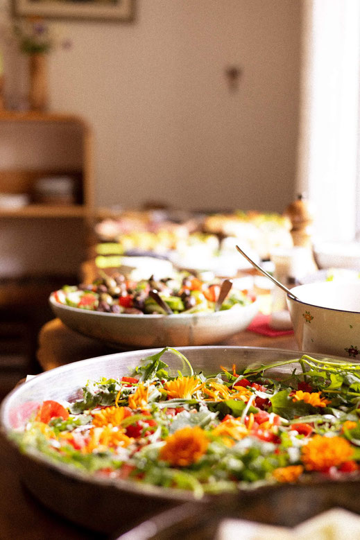 Große Schalen mit frischem gemischtem Salat, garniert mit essbaren Blüten, auf gedecktem Tisch