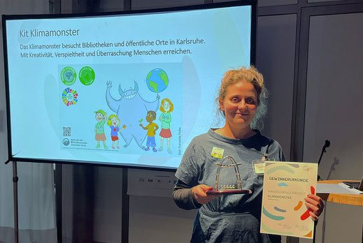 Franziska Poike steht mit einer Urkunde und Preis vor einer Leinwand über das Kit Klimamonster