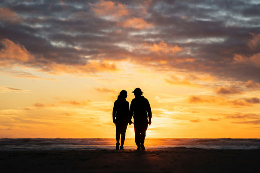 Mann und Frau halten sich an der Hand und sehen sich den Sonnenuntergang an