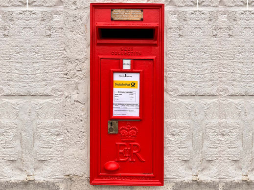 Photograph of a red British letterbox in a light-coloured natural stone wall