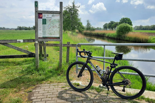 Ein Fahrrad steht an einem Fluss vor einem Schild mit einer großen Karte.