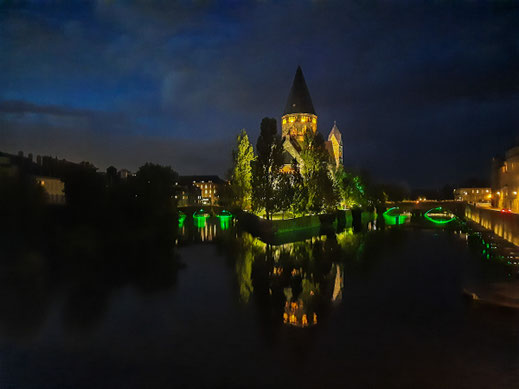 Eine Kirche auf einer Flussinsel wird nachts von gelben und grünen SCheinwerfern angestrahlt.