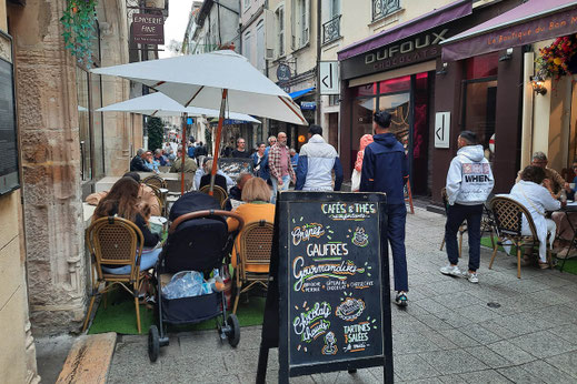 Menschen sitzen in einem Straßencafé in einer Altstadt. 
