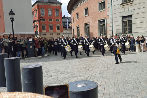 Ein Musikkorps mit blauen Uniformen marschiert durch eine enge Straße auf einen Platz.