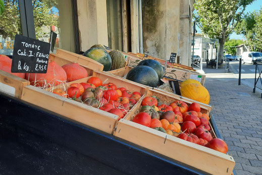 Vor einem Geschäft in einer französischen Altstadt stehen Kirsten mit frischem Obst.