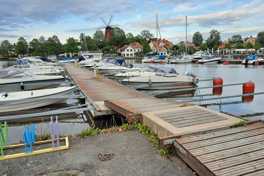 An den steegen des Freizeithafens von Strängnäs liegen viele Botte. Im Hintergrund ist eine alte Bockwindmühle zu sehen. 
