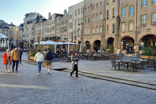 Menschen bummeln über einen Altstadt-Marktplatz. Vor einem Rstaurant stehen viele leere Tische.